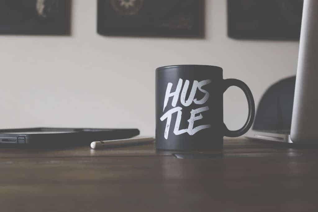 Ladybosses goals - black mug with white text that says Hustle sits on a desk next to an ipad